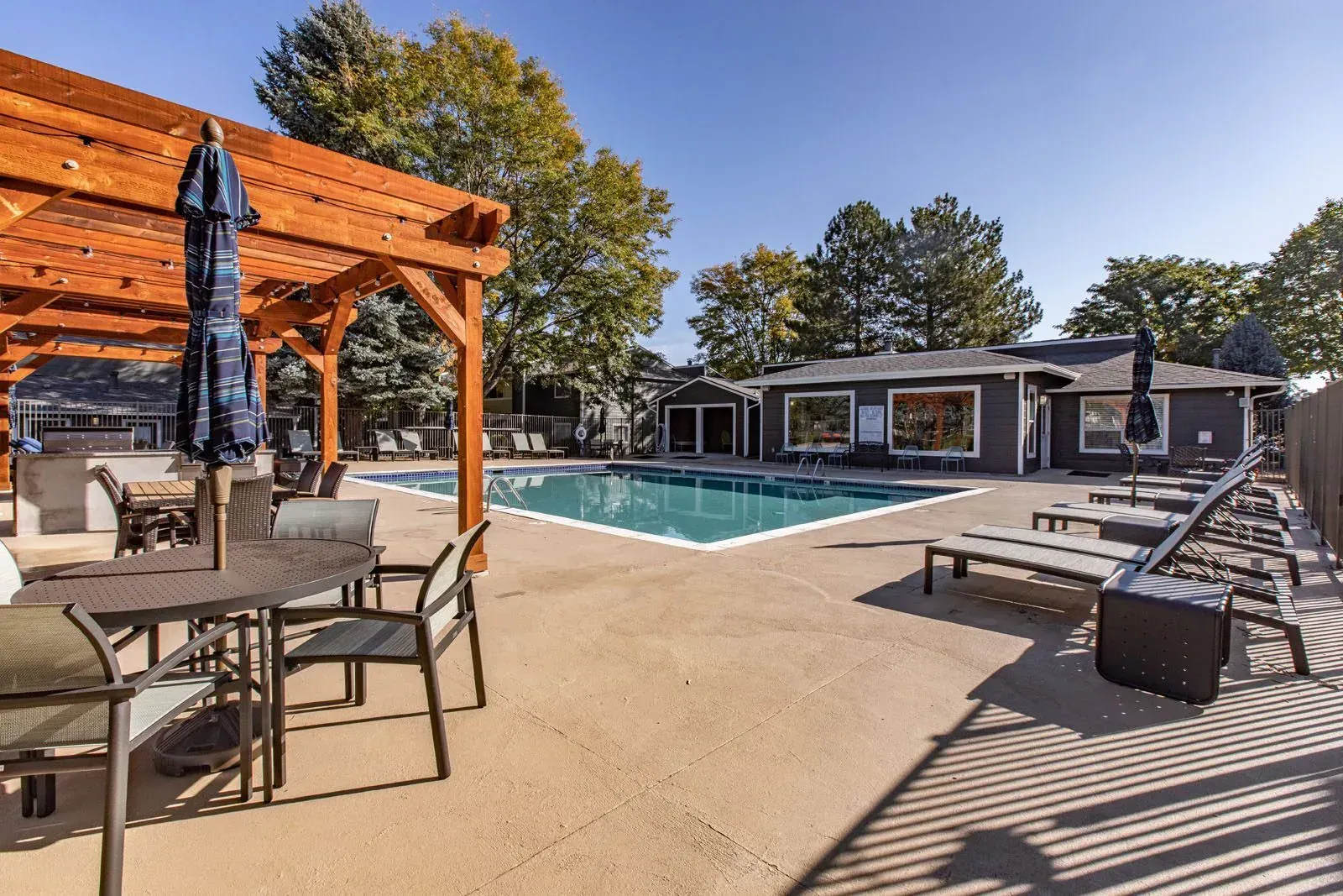 Pool area with tables, chairs, pergola, pool, and building at Westward Heights in Denver, CO.