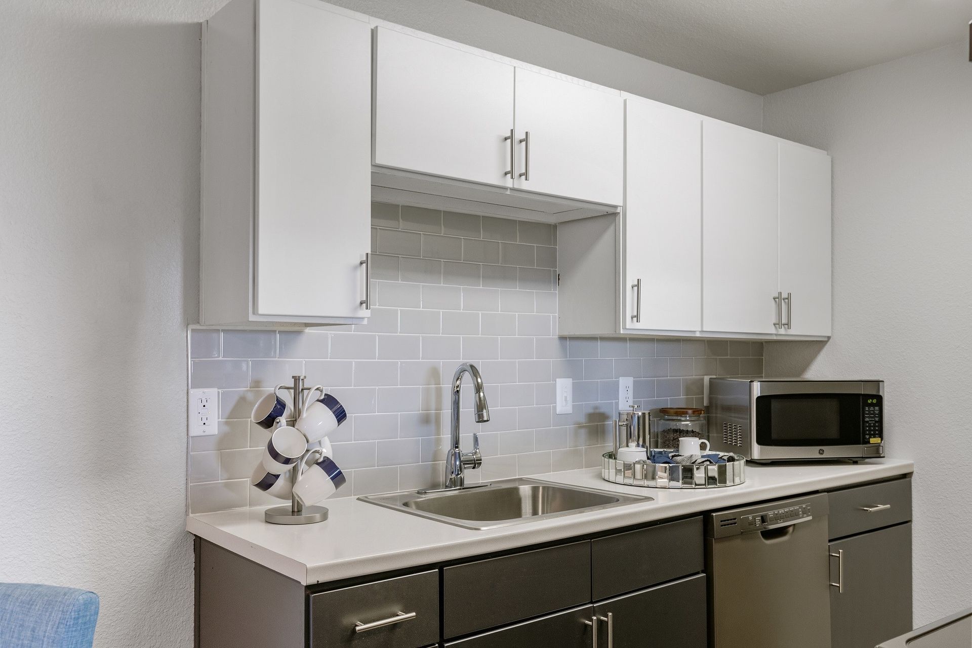 Small modern kitchen with white and dark gray cabinets, stainless steel appliances, and gray backsplash at Westward Heights in Denver, CO.