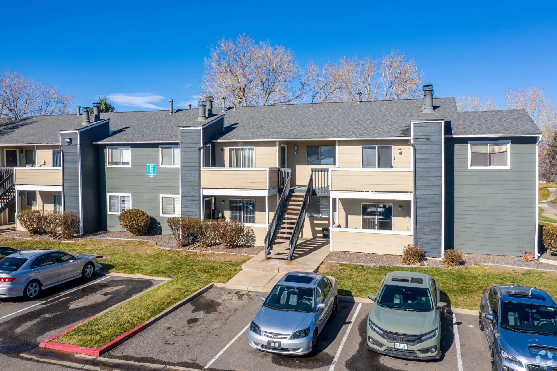 Two-story apartment building with parked cars in front. Gray siding and blue sky in the background at Westward Heights in Denver, CO.