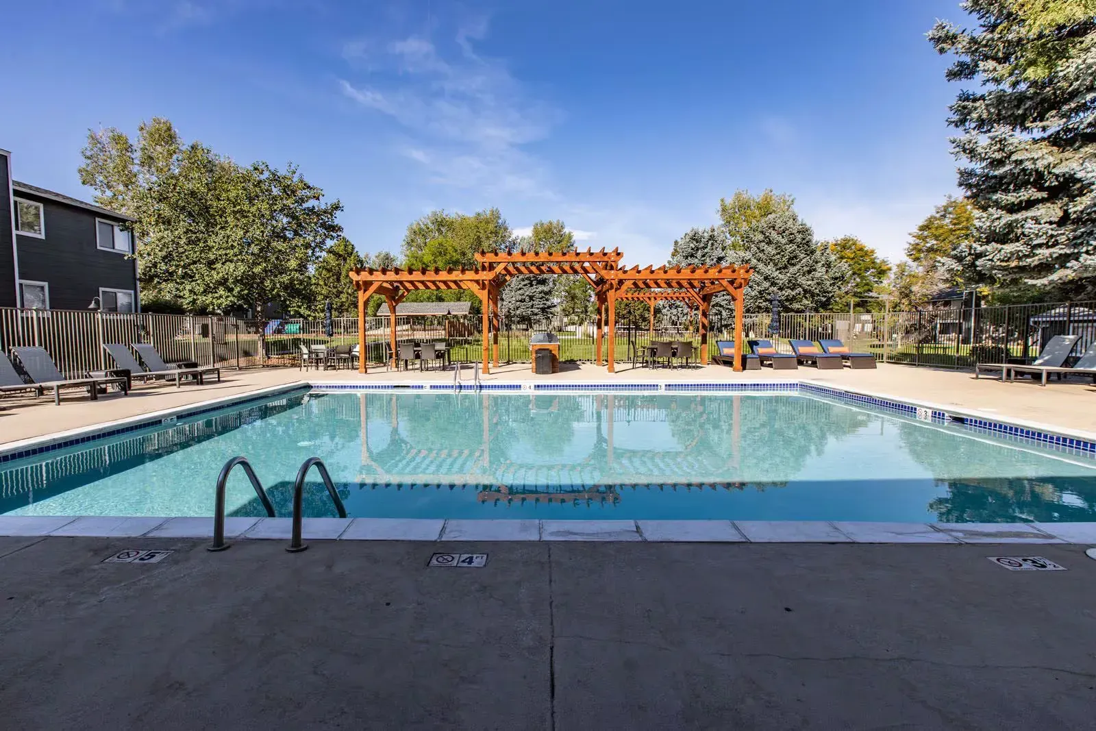 Swimming pool with lounge chairs, pergola, and trees under a blue sky at Westward Heights in Denver, CO.