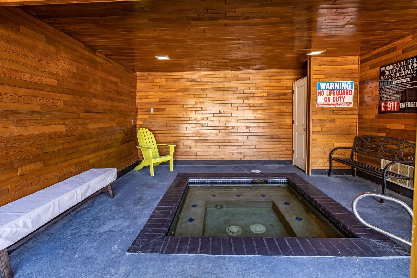 Indoor hot tub room with wood-paneled walls, a yellow chair, a bench, and a sign at Westward Heights in Denver, CO.