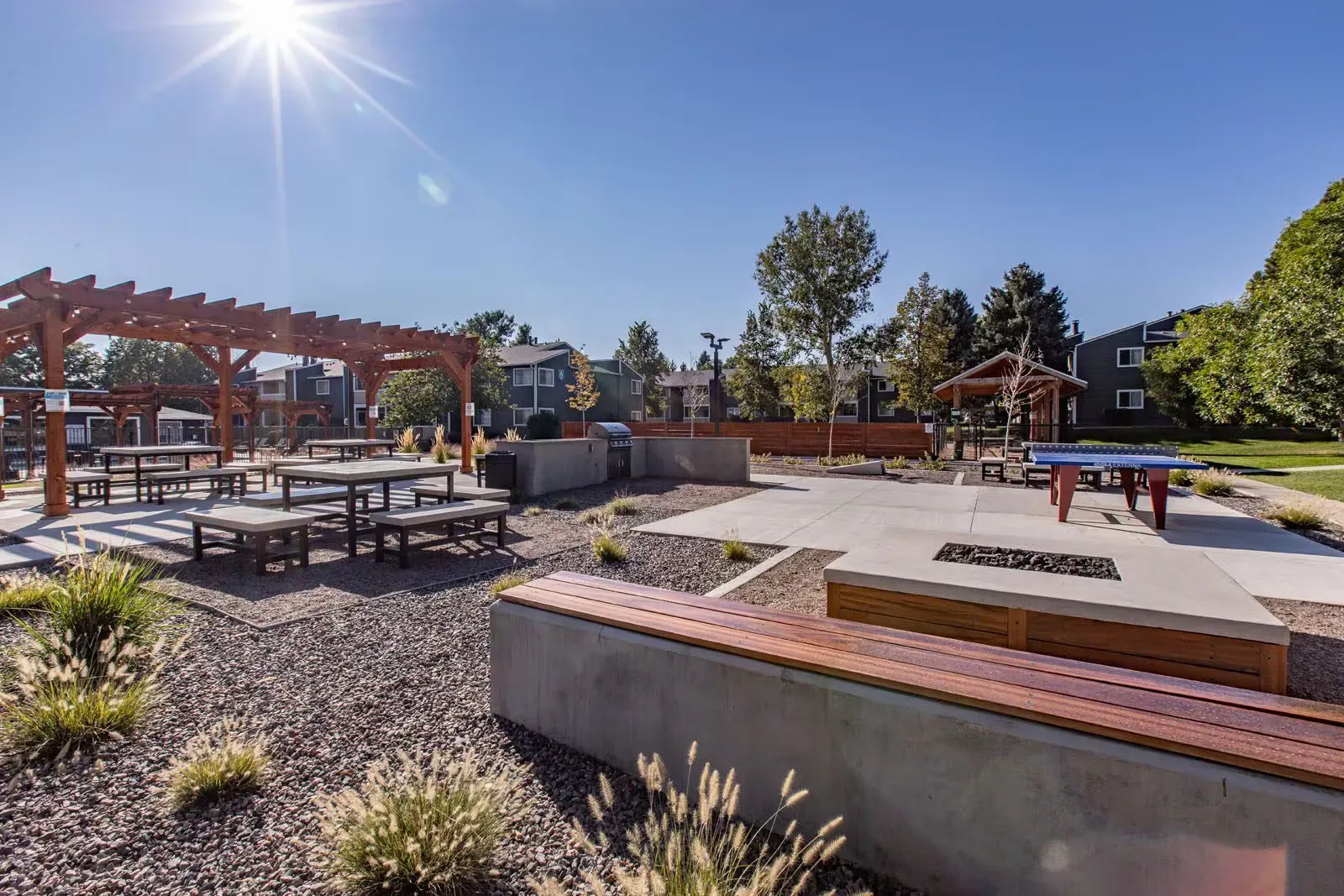 Outdoor patio with wooden pergolas, picnic tables, and concrete seating areas with fire pits on a sunny day at Westward Heights in Denver, CO.