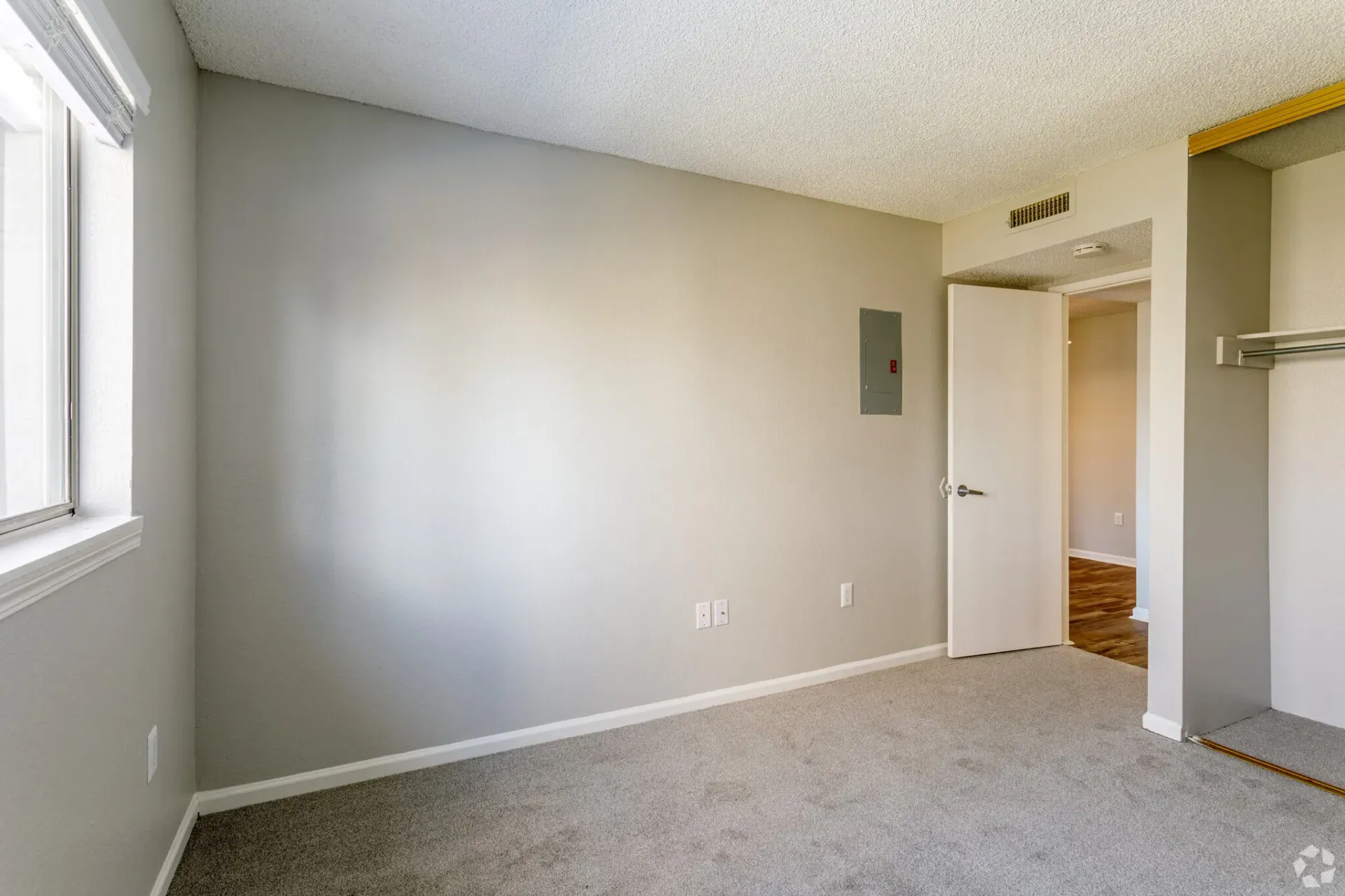 Empty bedroom with gray walls, carpet, window, and a door to another room at Westward Heights in Denver, CO.