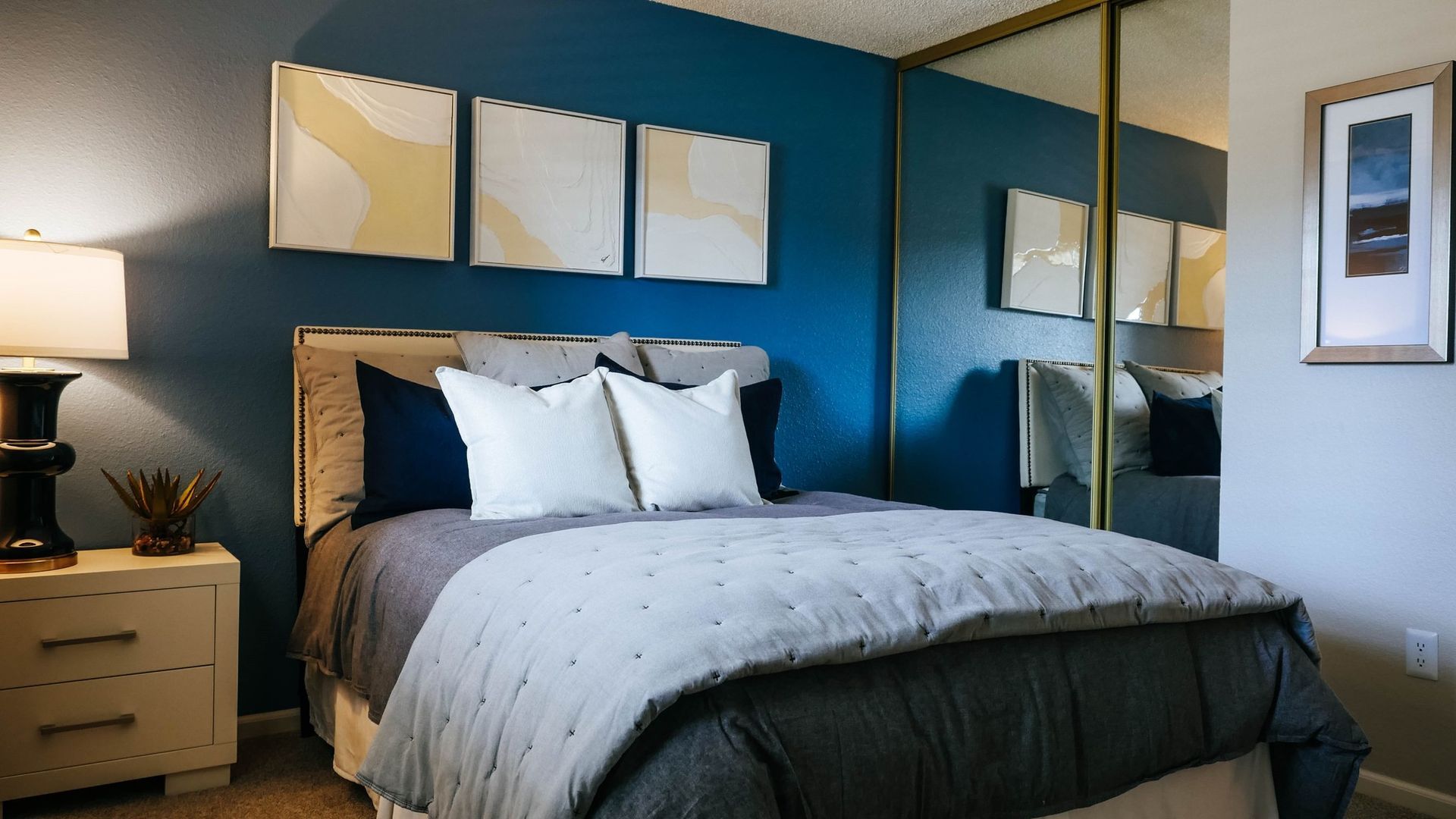 Bedroom with a blue wall, bed, nightstand, art, and mirror closet doors at Westward Heights in Denver, CO.