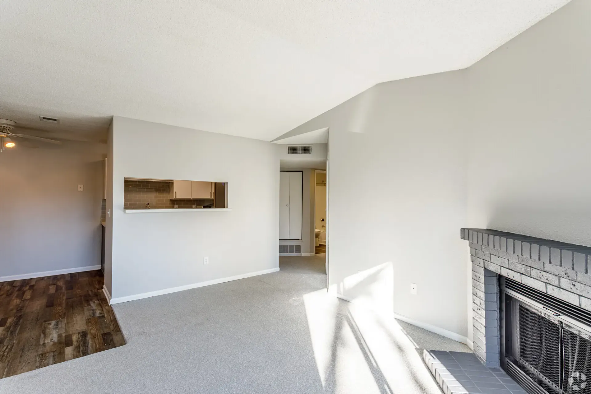 Empty living room with gray carpet, fireplace, and pass-through to kitchen at Westward Heights in Denver, CO.