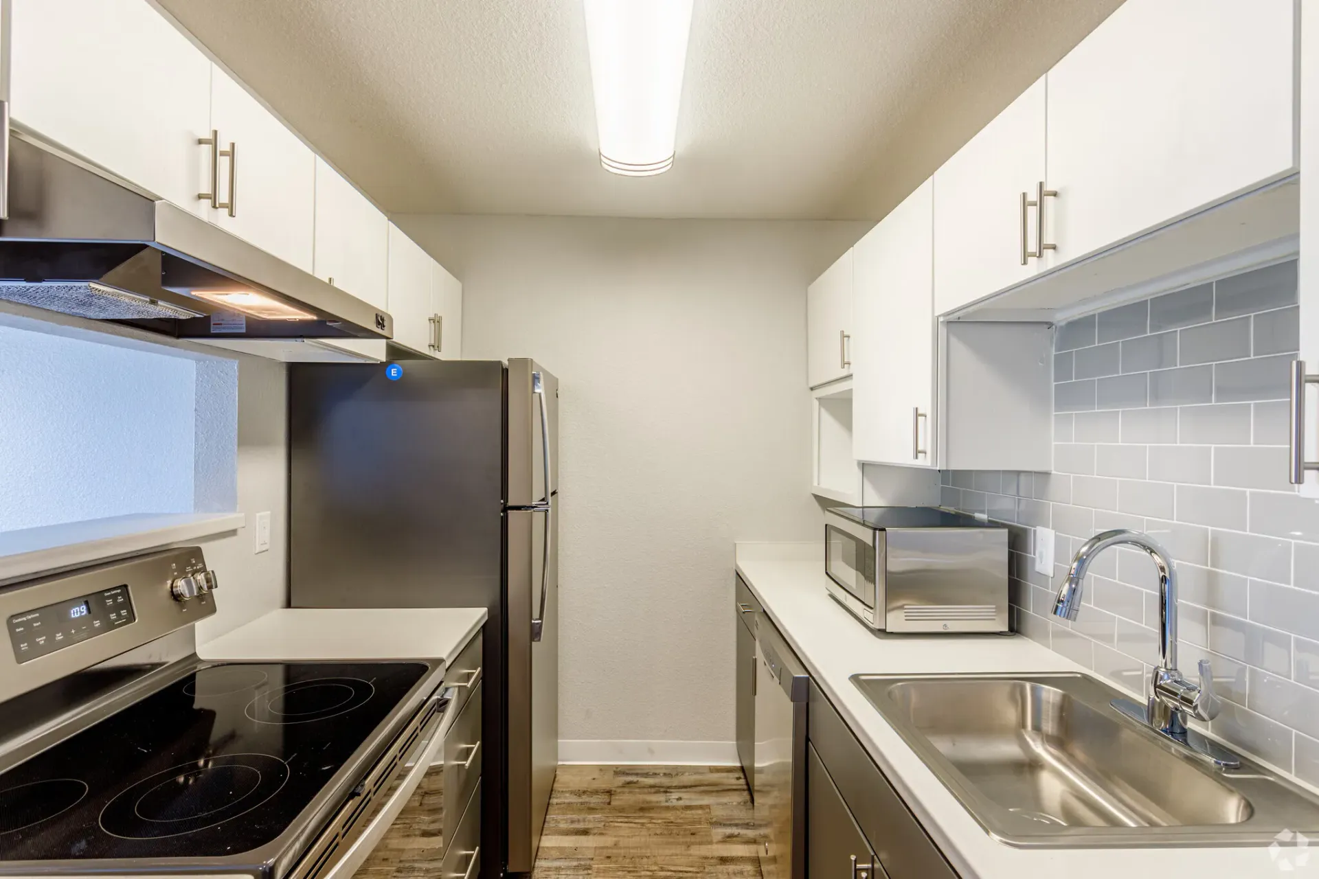 Modern galley kitchen with white cabinets, stainless steel appliances, and gray tile backsplash at Westward Heights in Denver, CO.