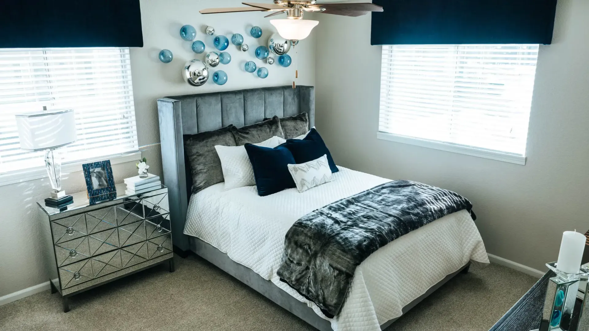 Bedroom with a bed, dresser, windows, and decorative wall art in blue and silver tones at Westward Heights in Denver, CO.