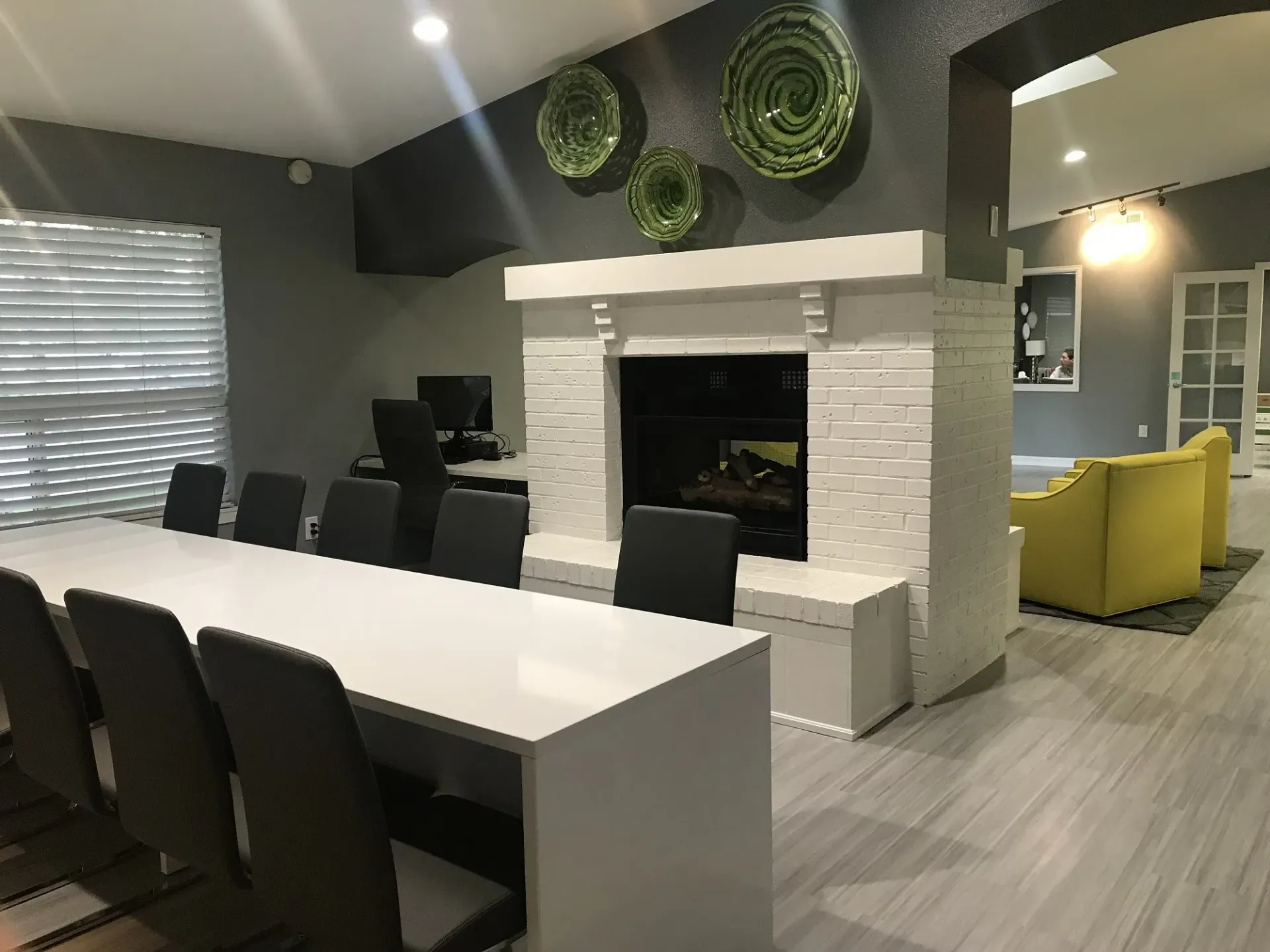 Lounge with a fireplace, long table with chairs, and yellow armchairs. Light gray walls, green wall decor at Westward Heights in Denver, CO.