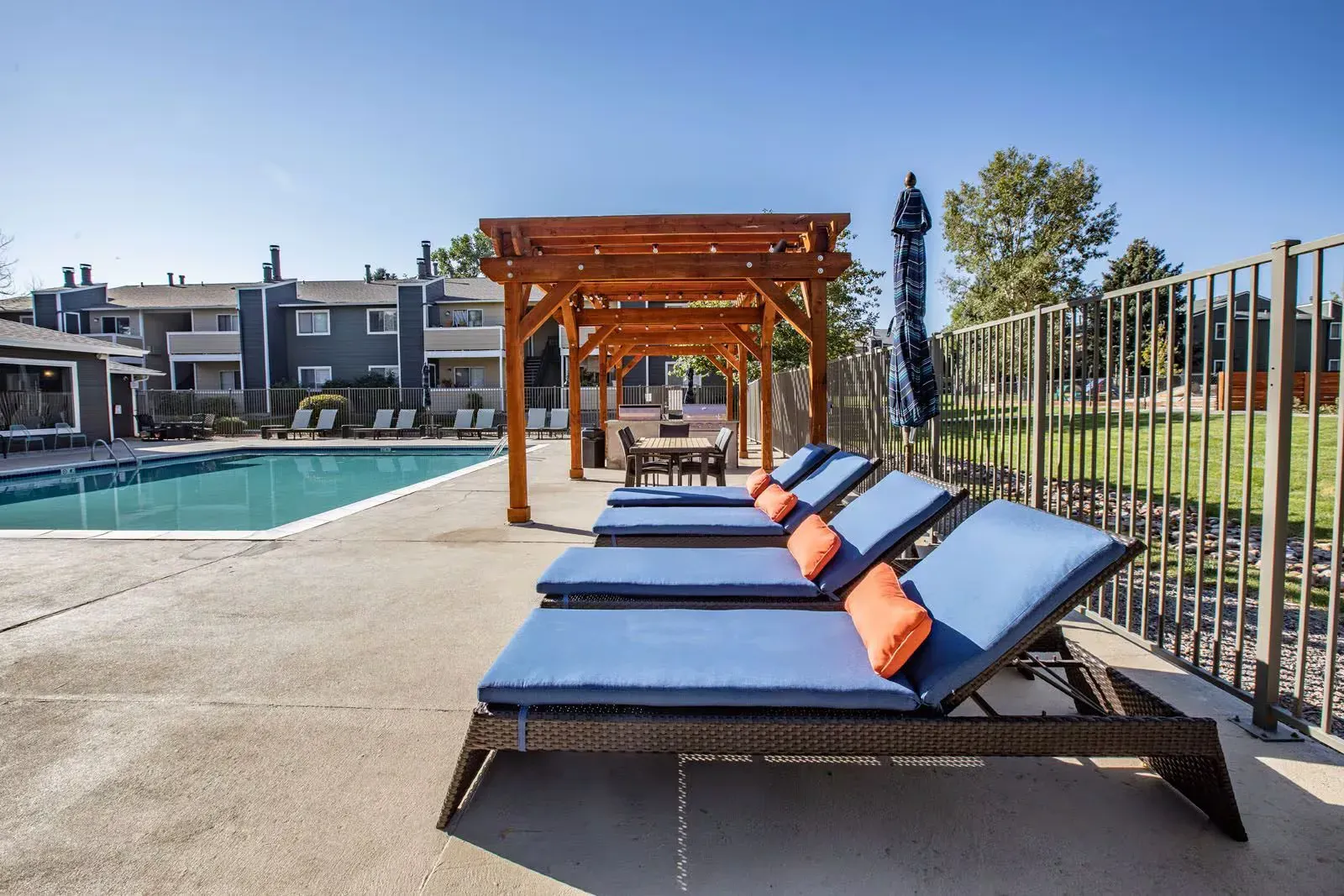 Poolside scene with lounge chairs, a pergola, and apartment buildings on a sunny day at Westward Heights in Denver, CO.