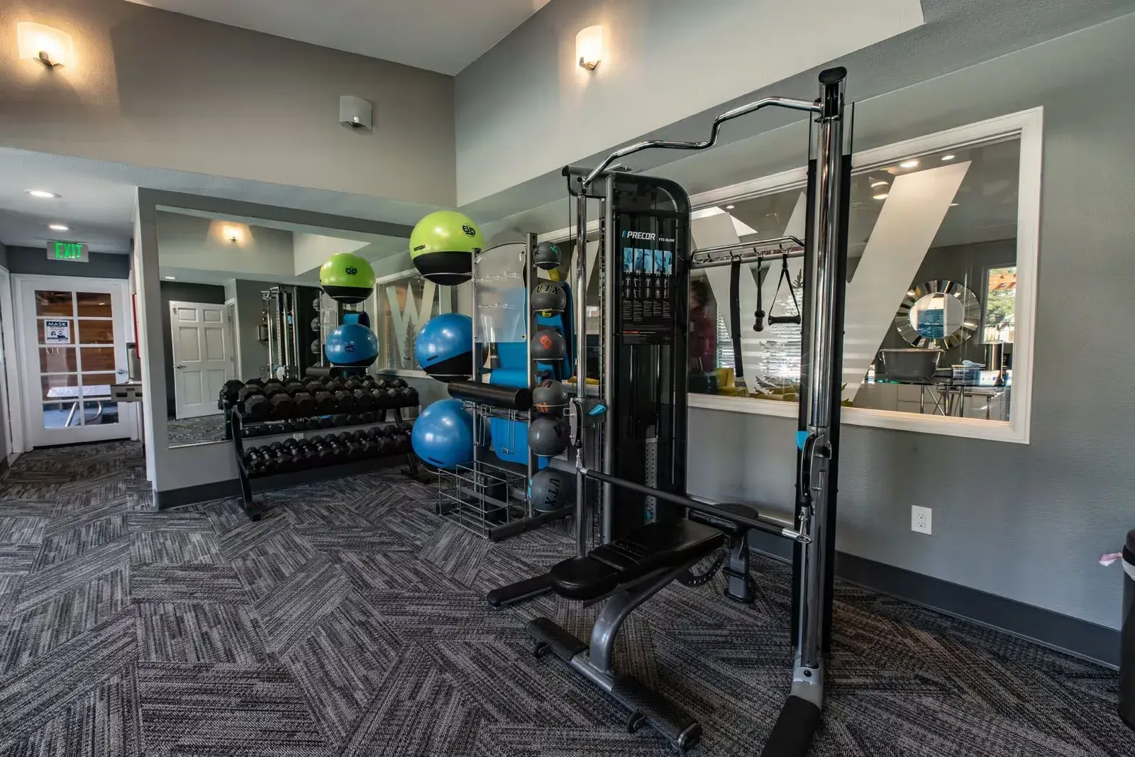 Gym with weights, exercise balls, and a multi-station machine; gray walls, carpet, and mirrors at Westward Heights in Denver, CO.