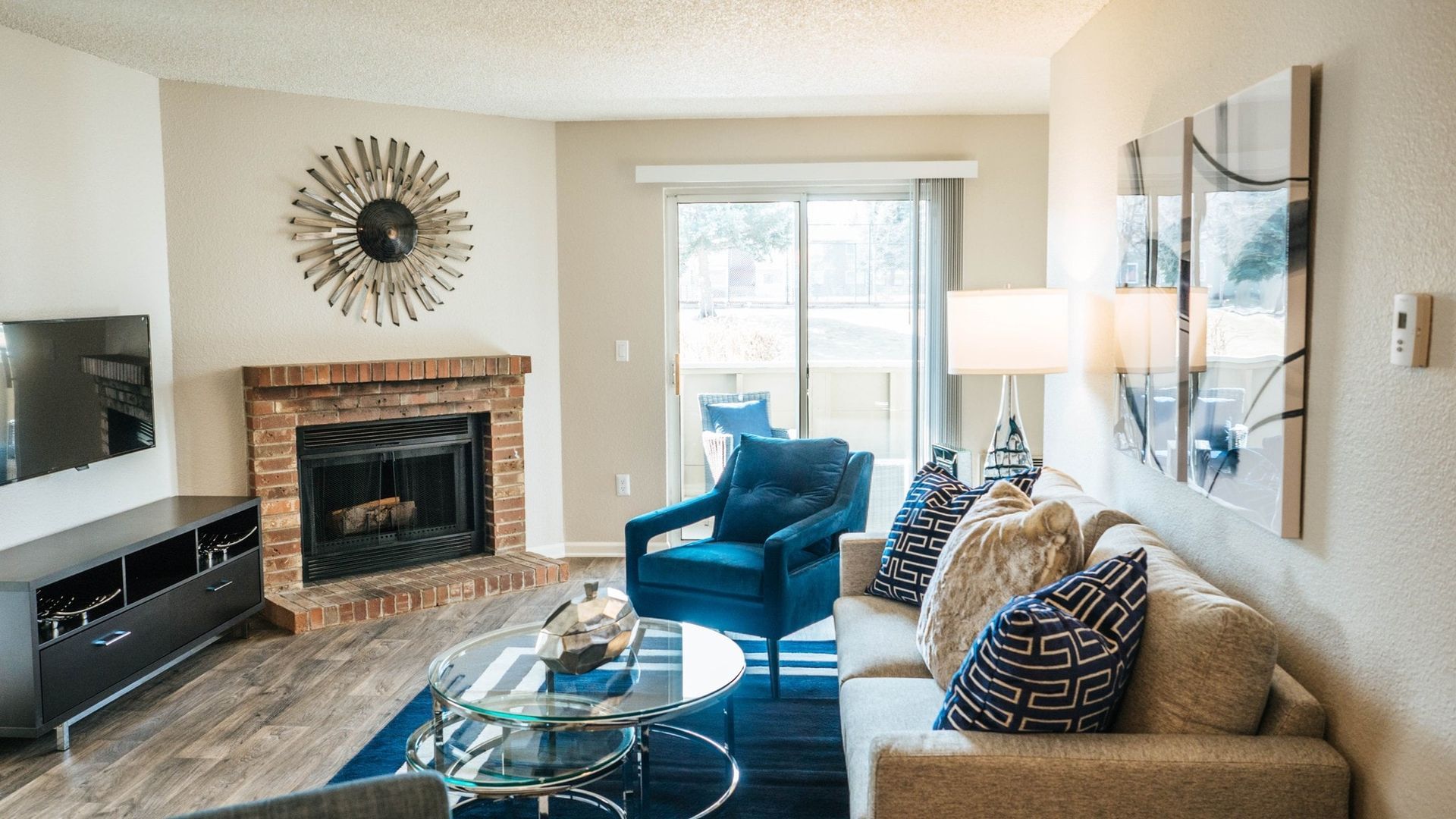 Living room with fireplace, blue armchair, cream sofa, glass coffee table, and sliding door at Westward Heights in Denver, CO.