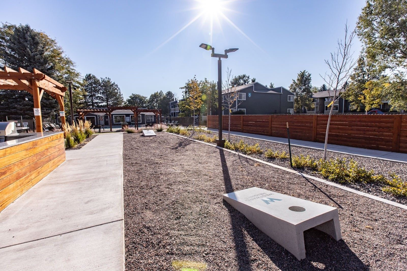 Outdoor recreation area with cornhole boards on gravel, lit by the sun at Westward Heights in Denver, CO.