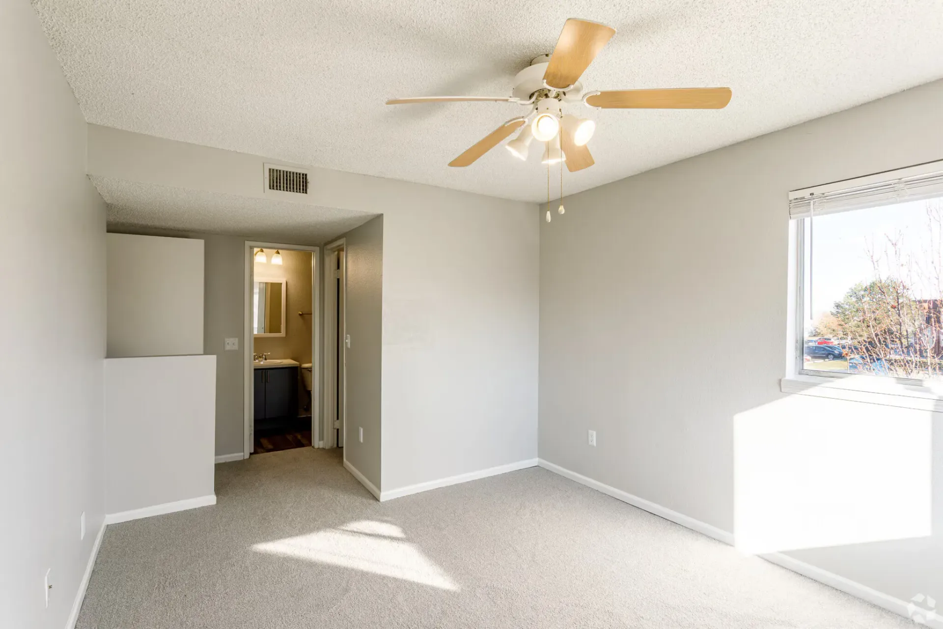 Bedroom with gray walls, carpet, ceiling fan, and window. Doorway leads to bathroom at Westward Heights in Denver, CO.