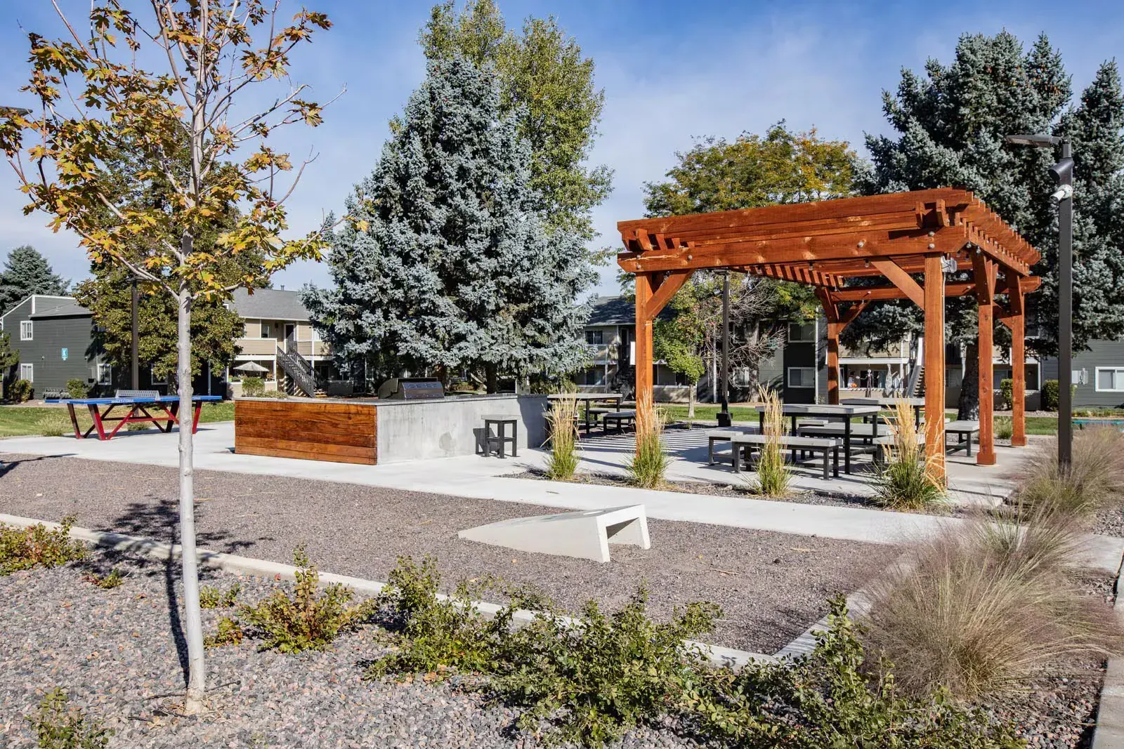 Outdoor recreational area with a wooden pergola, picnic tables, and landscaping under a blue sky at Westward Heights in Denver, CO.