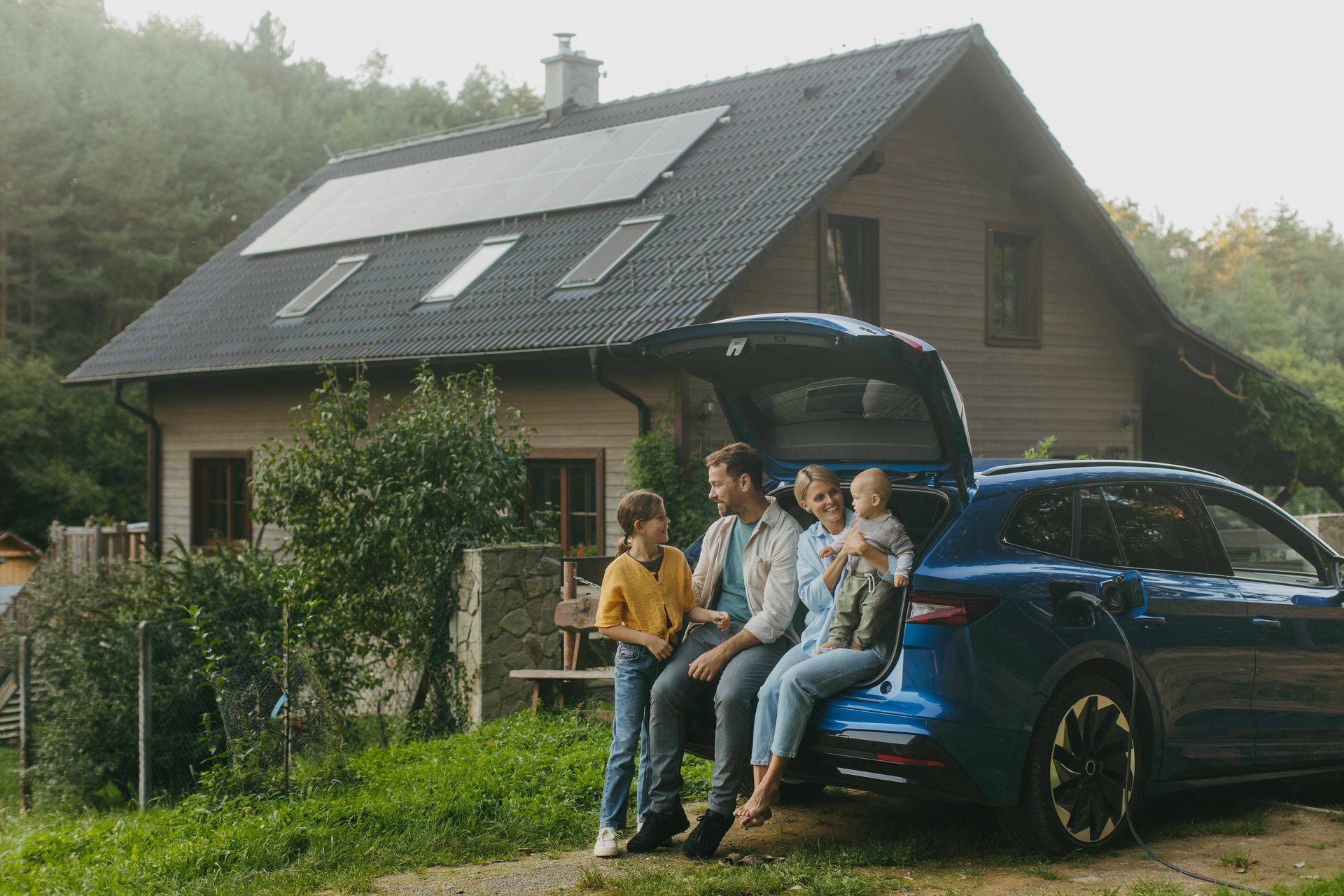 A family is sitting on the back of a car in front of a house.