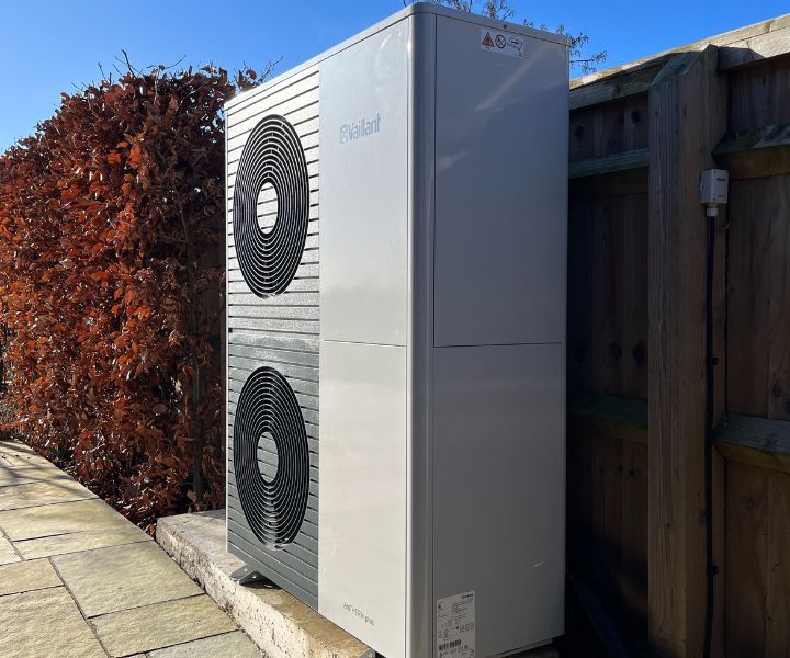 A large white air conditioner is sitting next to a wooden fence.