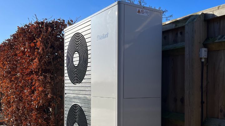 A large white air conditioner is sitting next to a hedge.