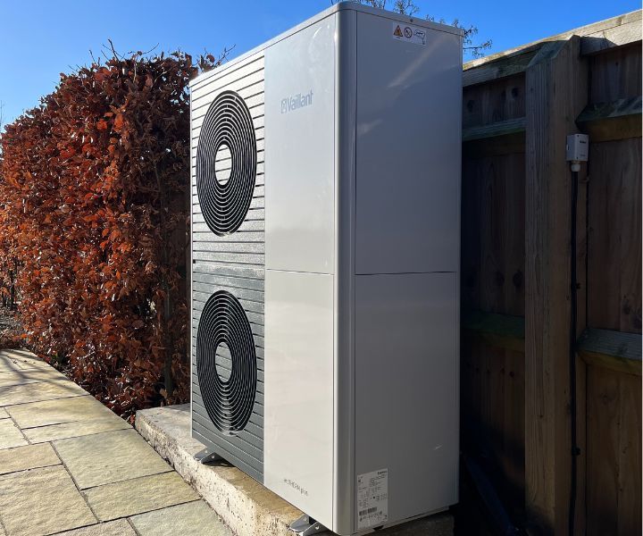 A large white air conditioner is sitting next to a wooden fence.