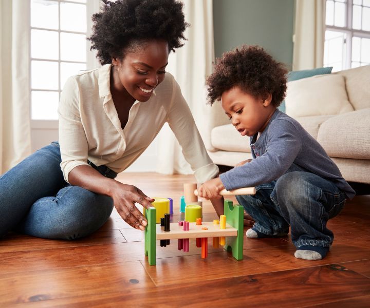 A woman and a child are playing with a wooden toy on the floor.