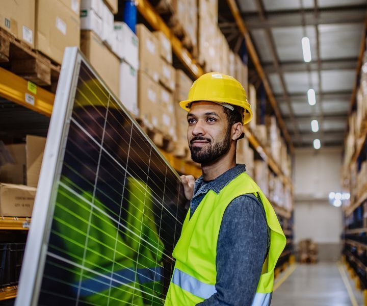 A man is holding a solar panel in a warehouse.