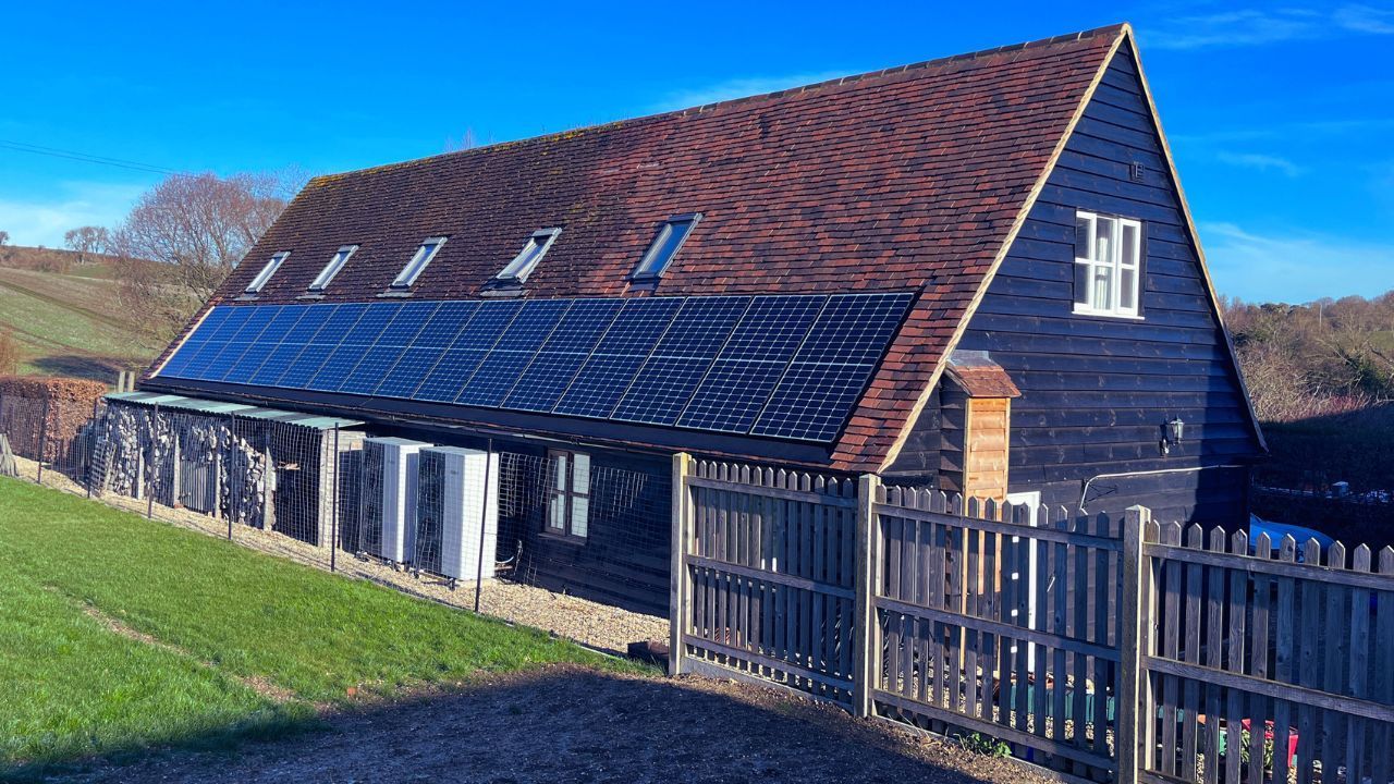 A large barn with solar panels on the roof and a wooden fence around it.