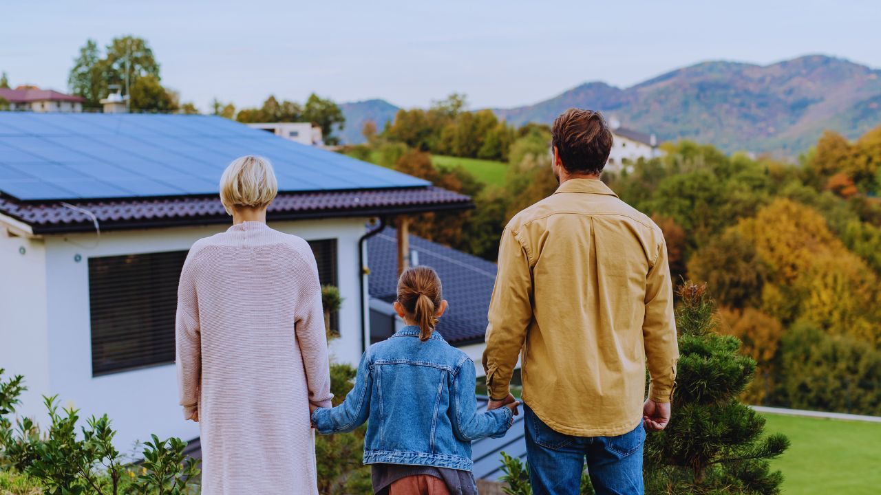 A family is standing in front of a house with solar panels on the roof.