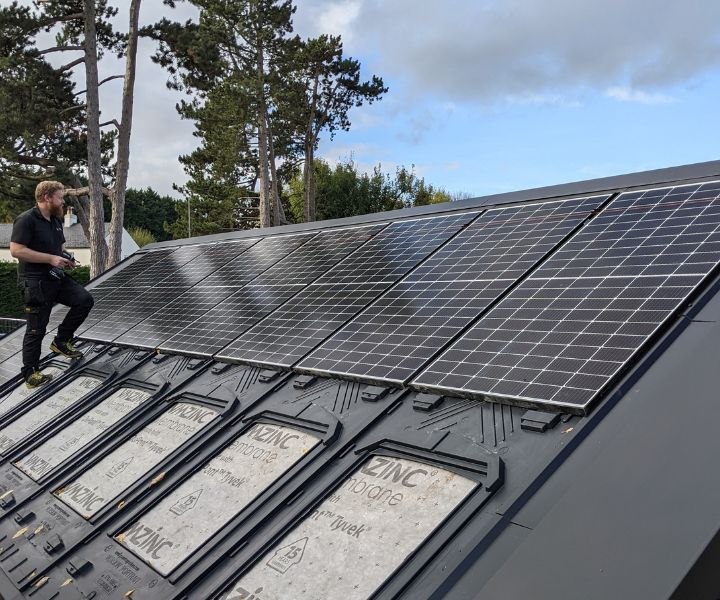 A man is standing on top of a roof with solar panels.