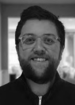 A man with a beard and glasses is smiling in a black and white photo.