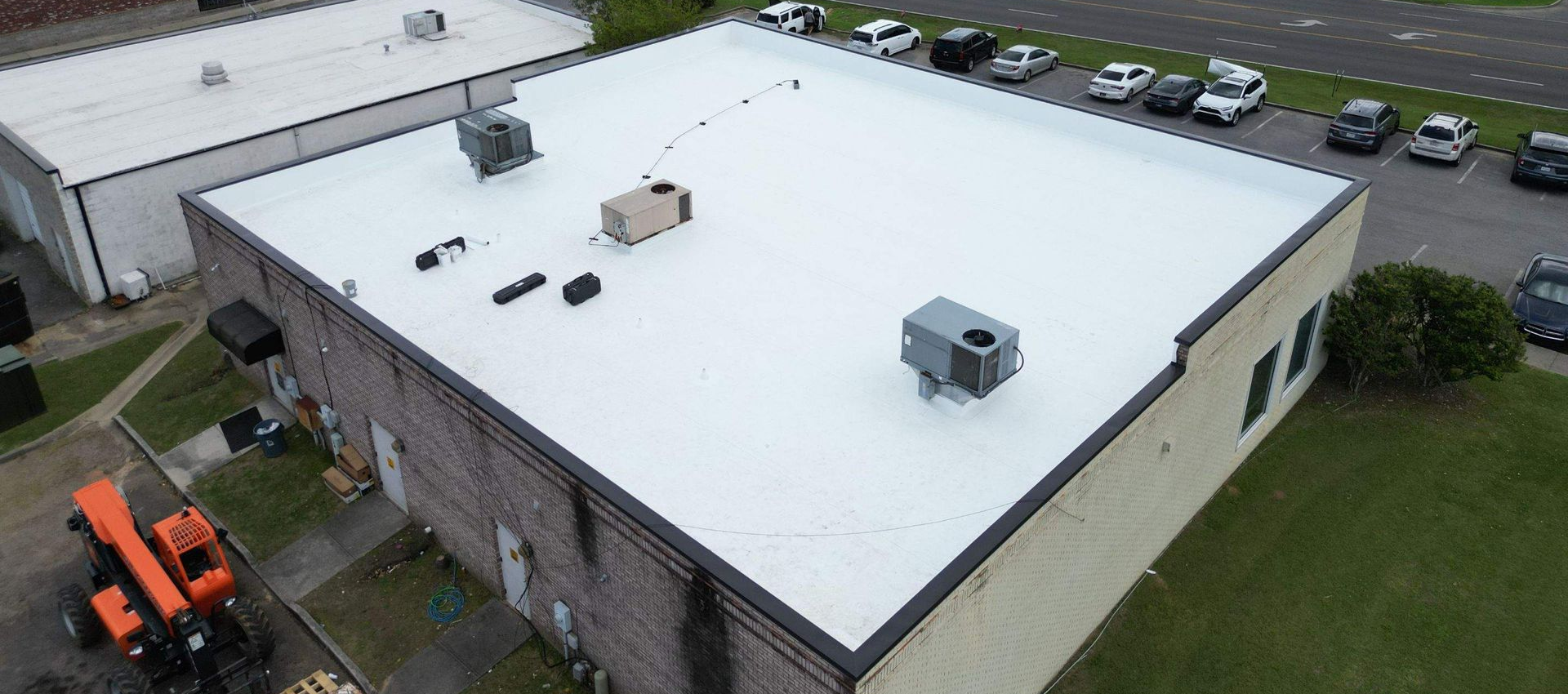 Aerial view of a white flat roof with equipment. Buildings, parking lot, and a lift in the foreground.