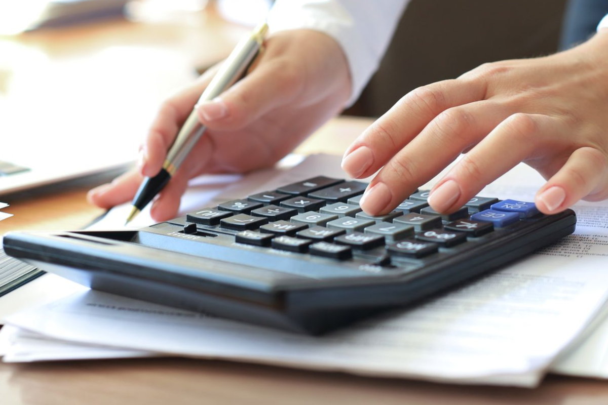 Person using a calculator with pen, working on paperwork at a desk.