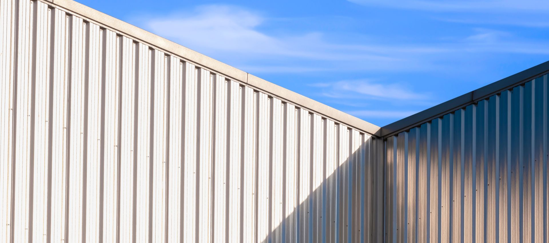 Corrugated metal walls meet at an angle against a blue sky.