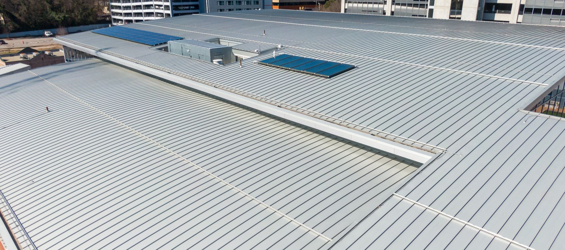 View of a large, curved metal roof with buildings in the background. Bright, sunny day.