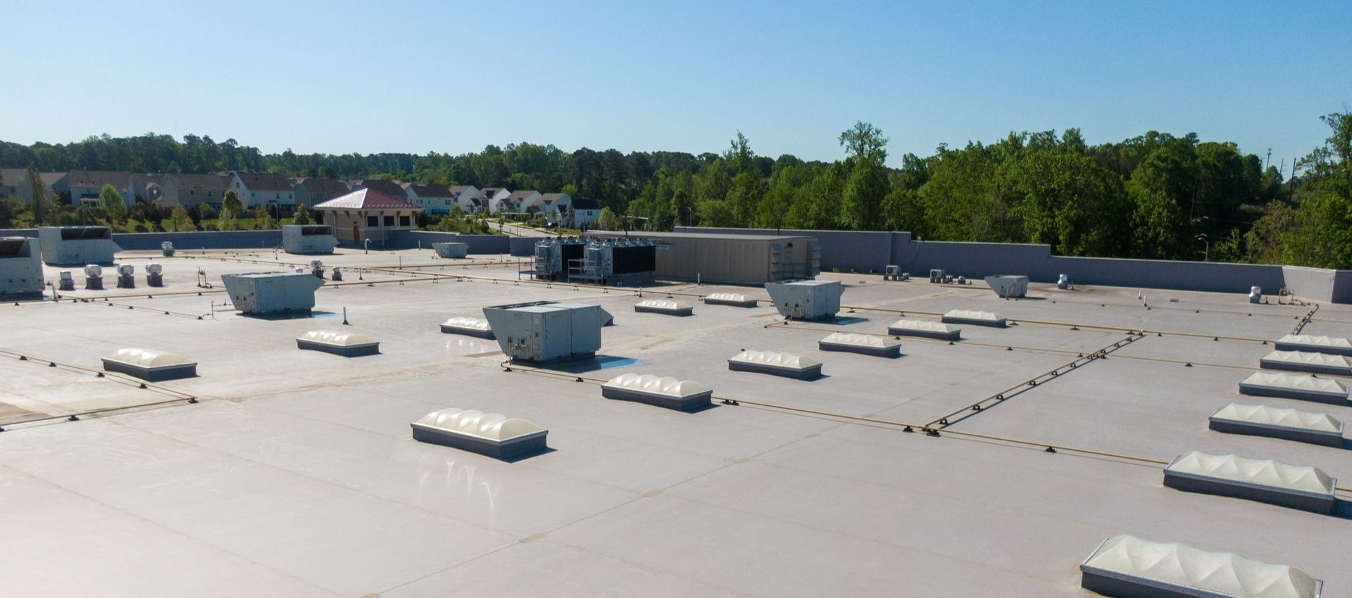 Flat commercial roof with skylights and vents under a blue sky.