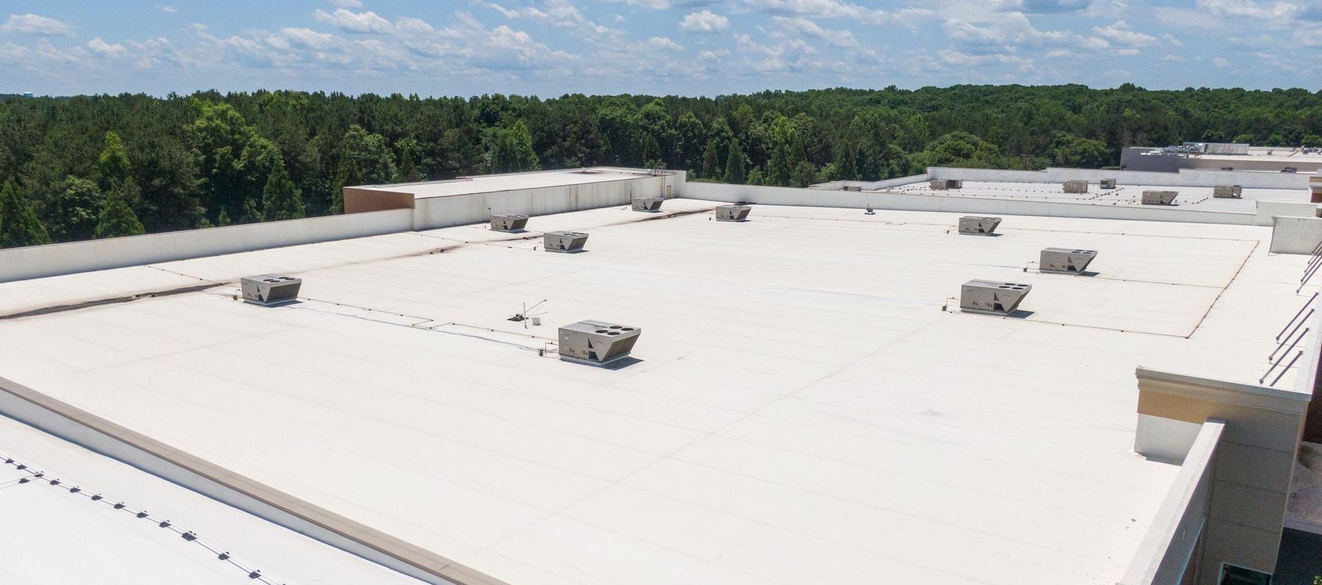 The roof of a building with a white roof and trees in the background.