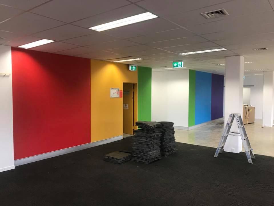 Colorful freshly painted walls in a hallway, with stacked tiles and a ladder on the dark floor.