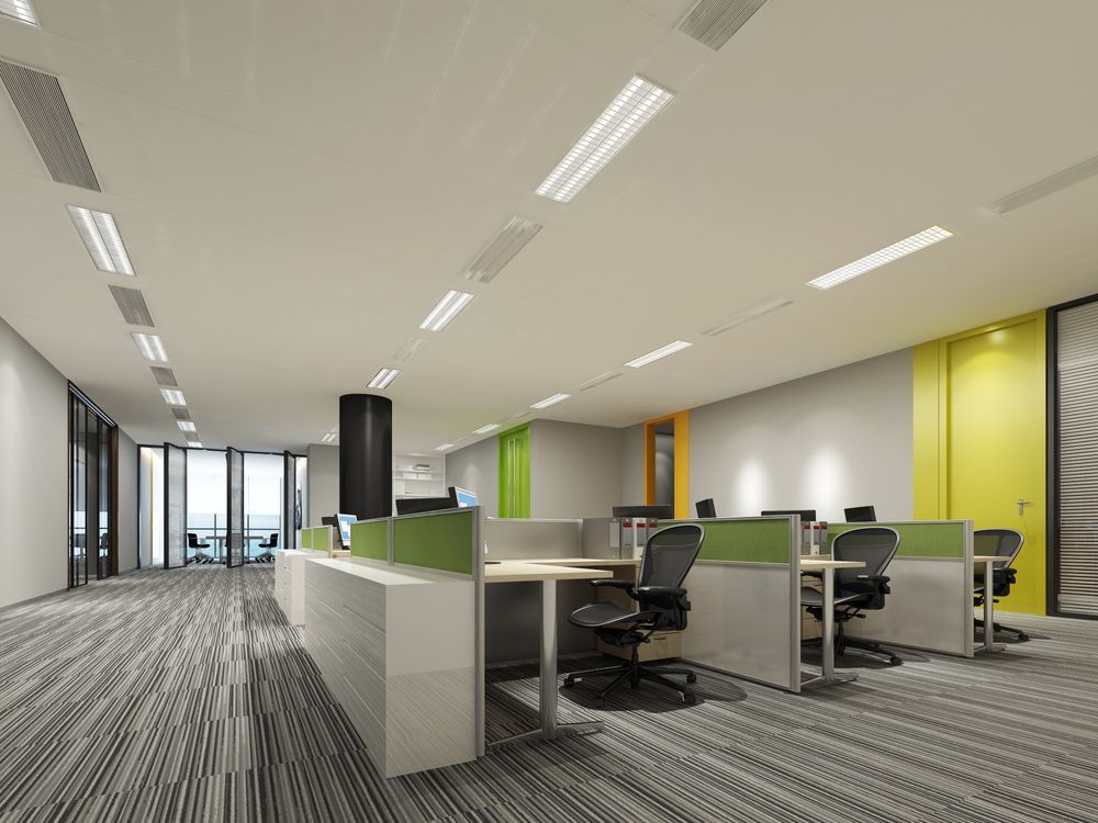 Modern office interior with cubicles, desks, and carpeted floors; overhead lighting.