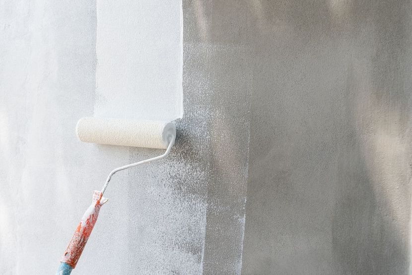 A paint roller applying white paint to a concrete wall, leaving a painted stripe.