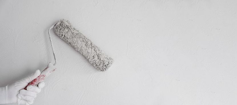 A paint roller applying white paint to a concrete wall, leaving a painted stripe.