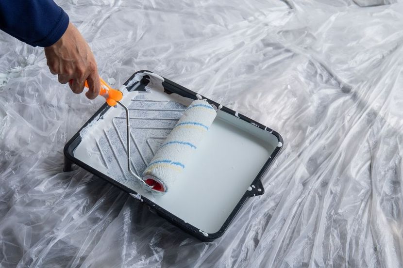 A paint roller applying white paint to a concrete wall, leaving a painted stripe.