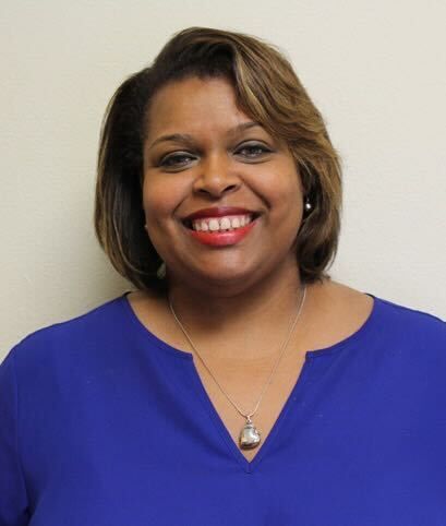Woman with short, layered brown hair, smiling, wearing a blue top, and a necklace.