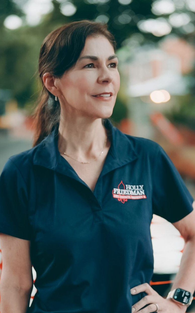 Woman in a navy polo shirt with "Kelly Paden" logo, hands on hips, looking off-camera.
