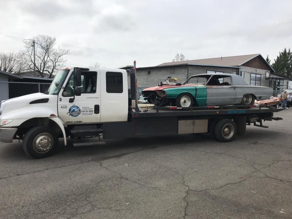 A tow truck with two cars on the back is parked in a parking lot.