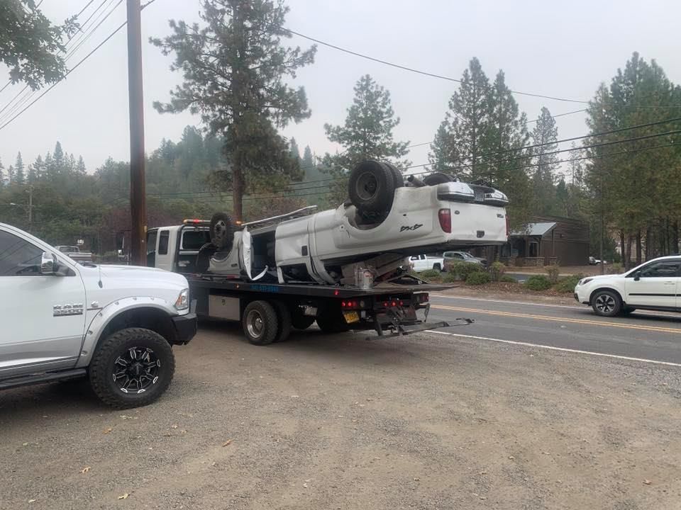 A white truck is being towed down the road by a tow truck.