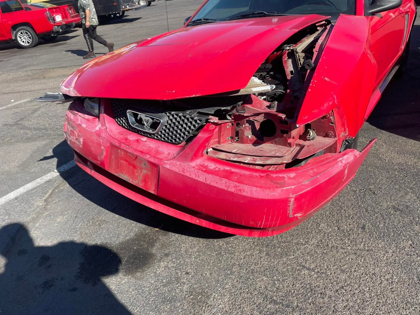A red car with its hood open is parked in a parking lot.