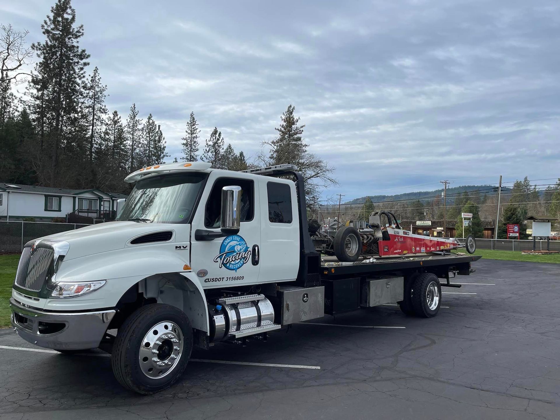 A white tow truck with a red car on the back is parked in a parking lot.