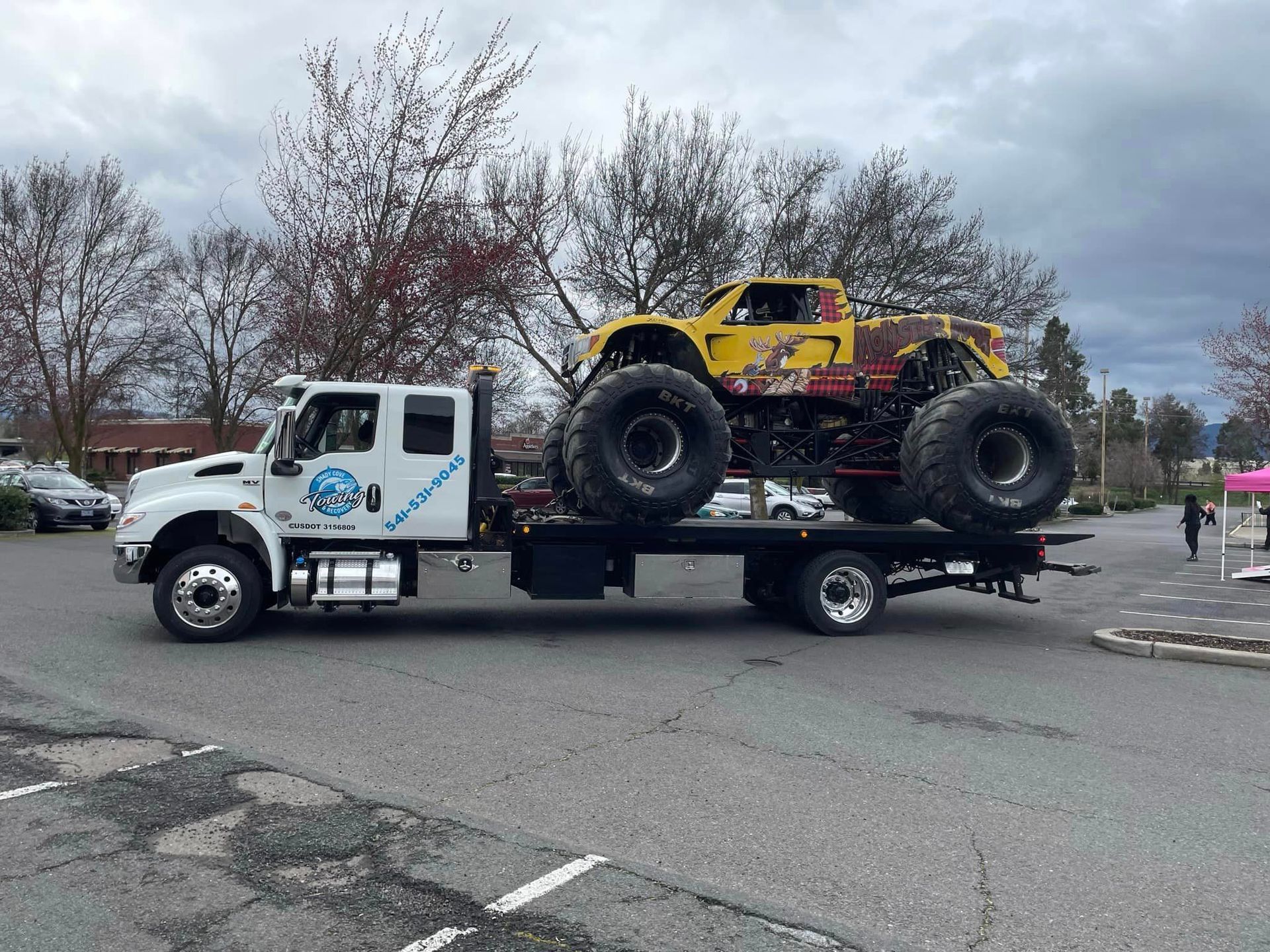 A monster truck is being towed by a tow truck in a parking lot.
