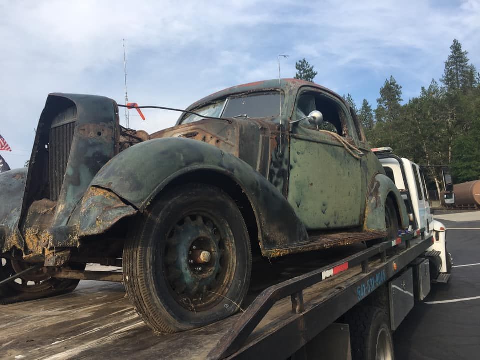 An old car is being towed by a tow truck.