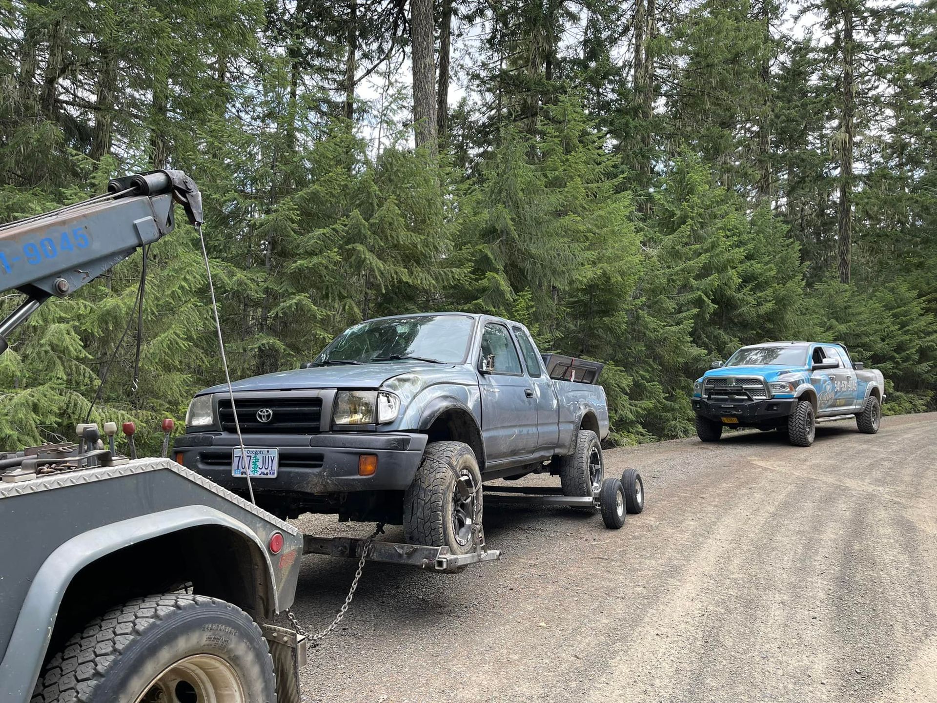 A truck is being towed down a dirt road by a tow truck.