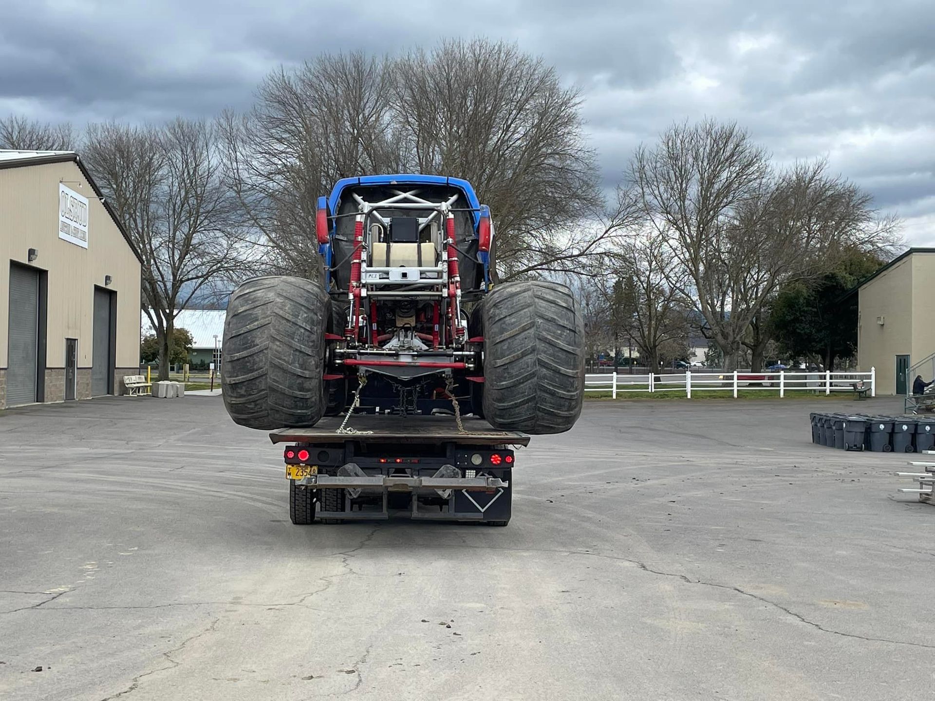 A monster truck is being towed by a tow truck in a parking lot.