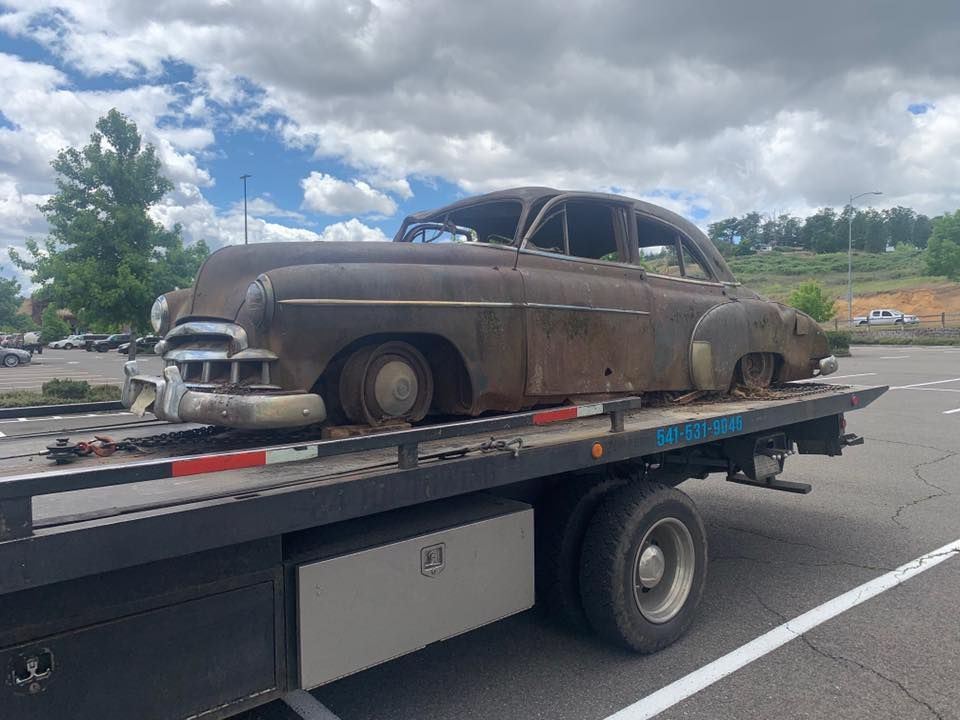 An old rusty car is being towed by a tow truck.